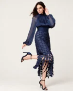 Plano em movimento da modelo com vestido longo em tule azul-marinho destacando mangas transparentes e barra com acabamento vazado.