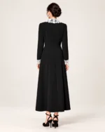 Modelo vestindo vestido midi evasê preto com gola e punhos de renda branca em estúdio mineral