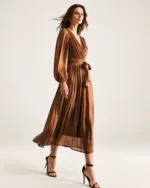 Plano inteiro da modelo caminhando com vestido midi plissado bronze em estúdio mineral