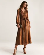 Plano frontal da modelo vestindo vestido midi plissado bronze em estúdio mineral
