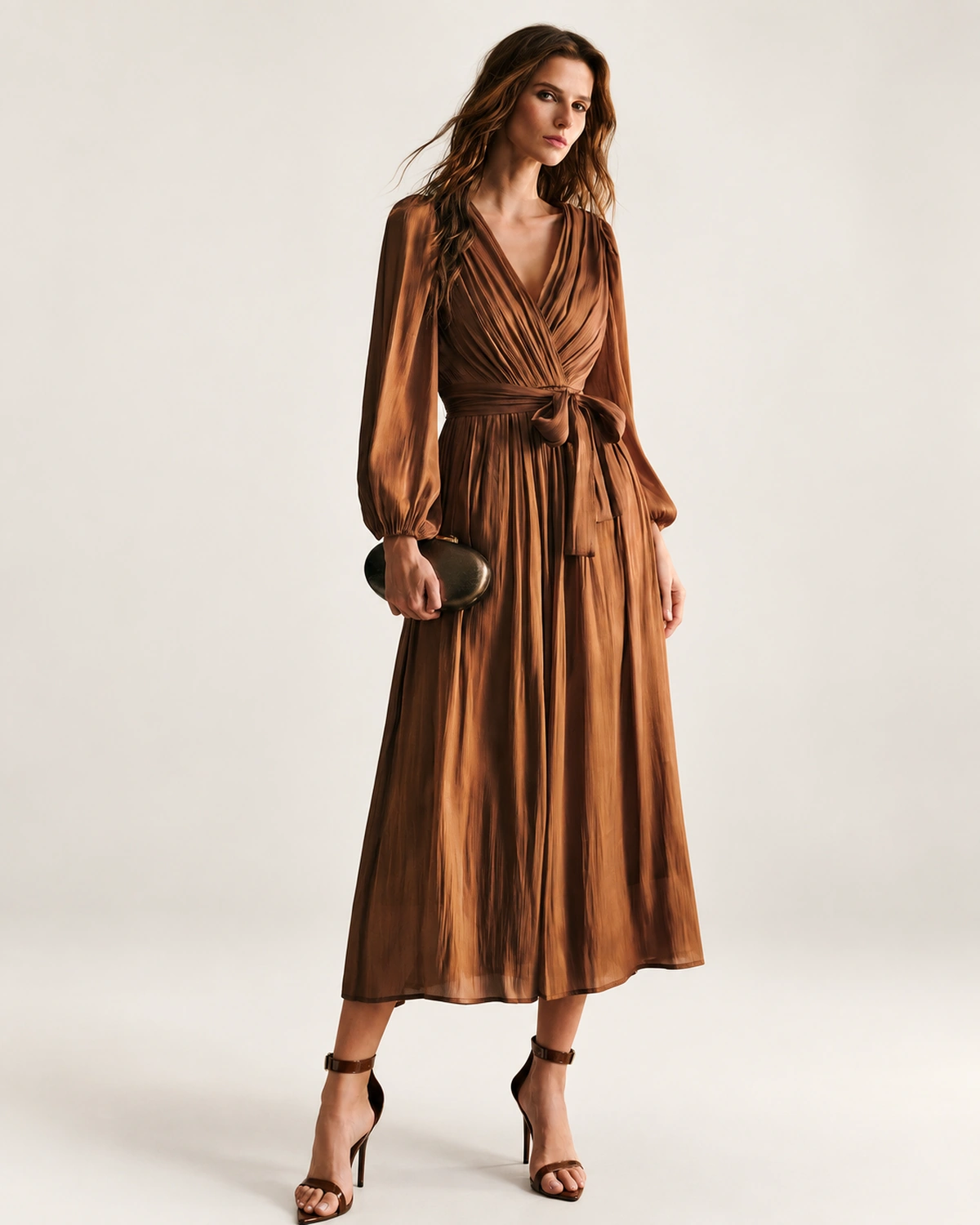 Plano frontal da modelo vestindo vestido midi plissado bronze em estúdio mineral