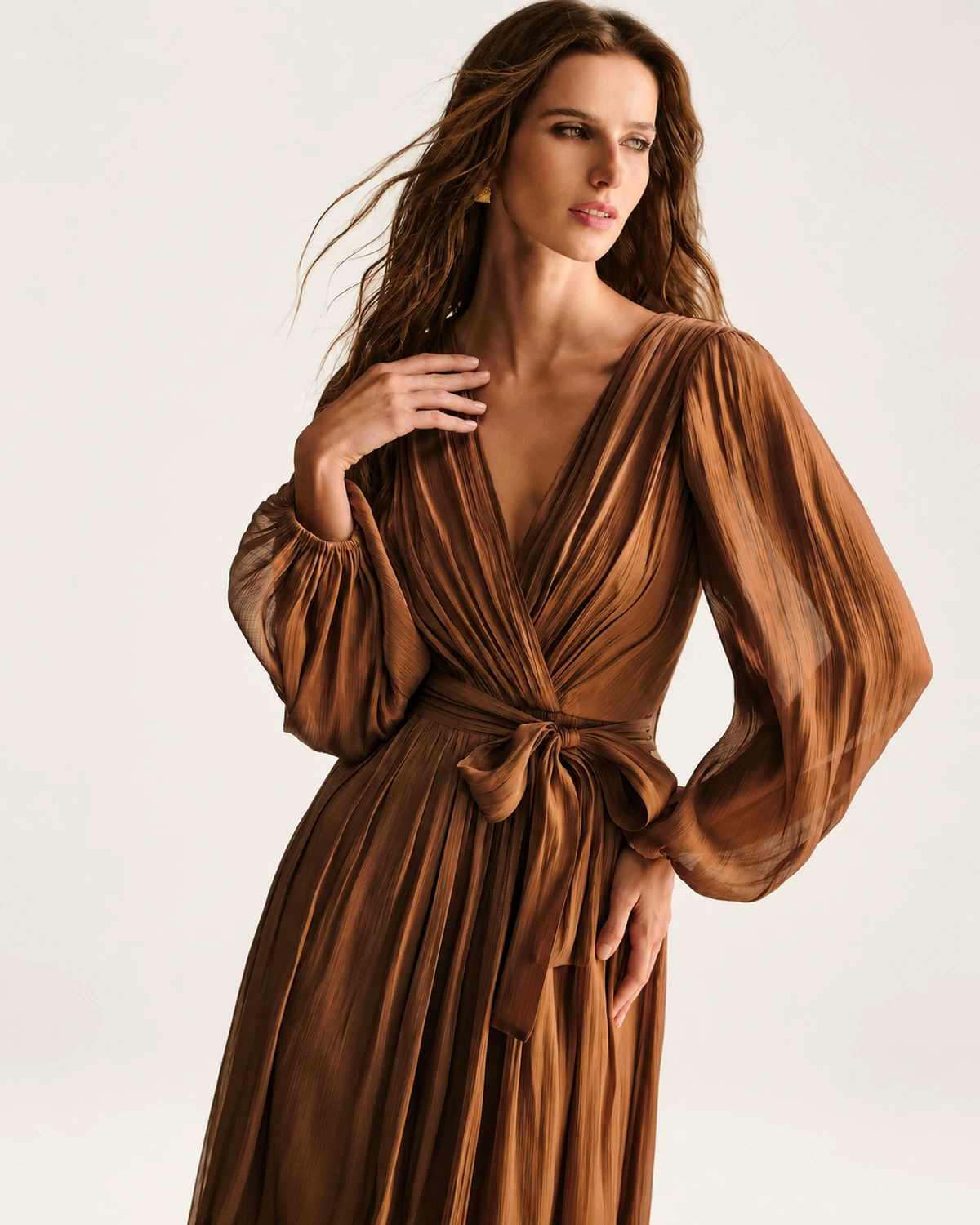 Plano médio destacando a leveza das mangas bispo em chiffon plissado bronze em estúdio mineral