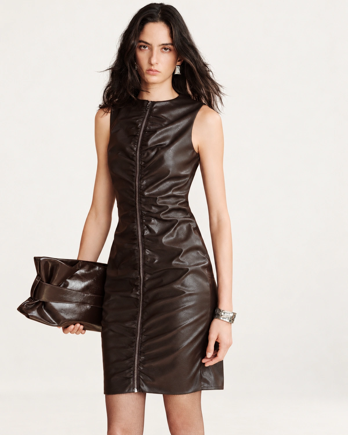 Plano médio da modelo vestindo vestido em couro marrom com clutch