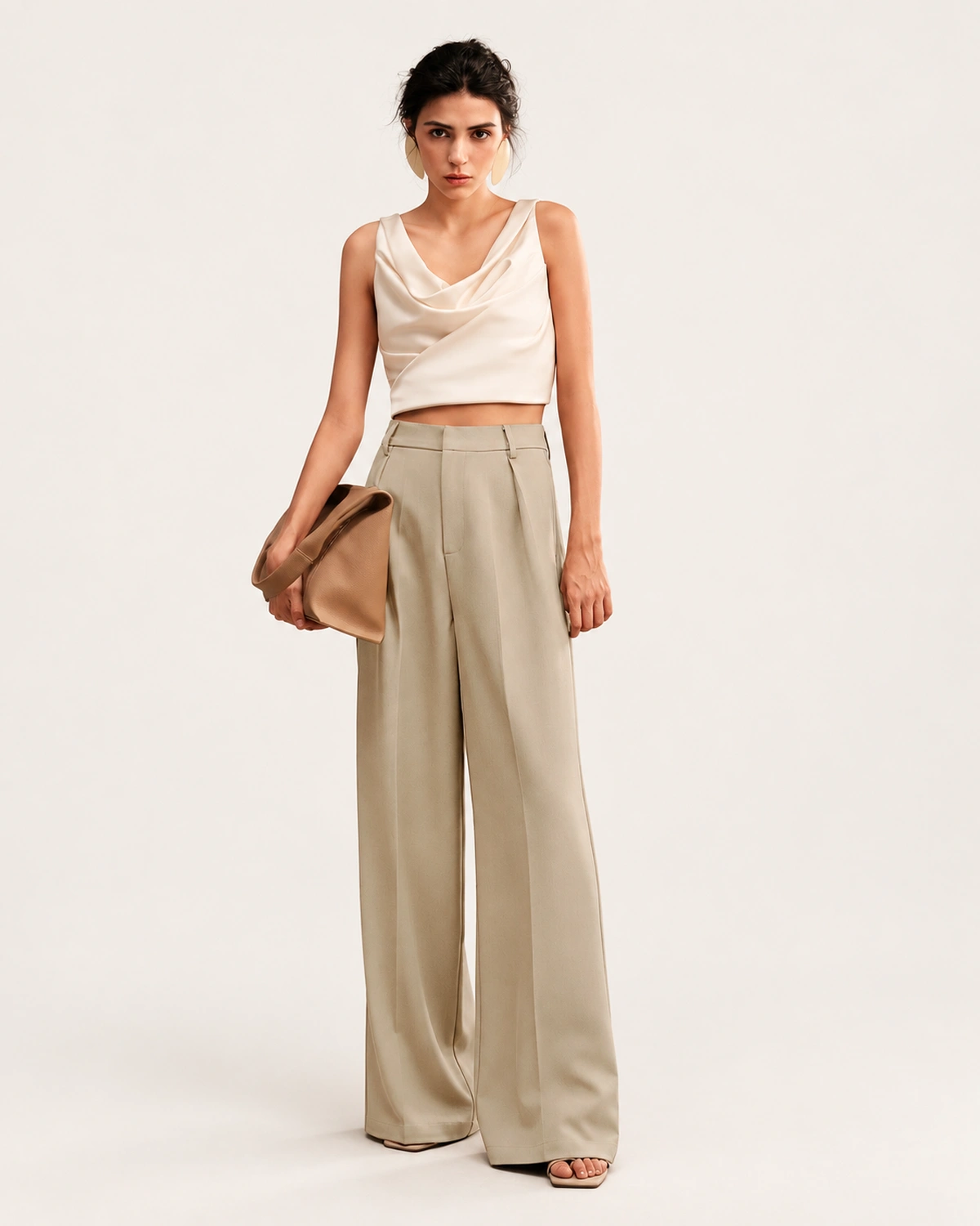 Modelo vestindo calça de alfaiataria reta com pregas e cós alto na cor Areia com top off-white em estúdio mineral