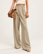 Modelo vestindo calça alfaiataria na cor Areia segurando clutch de couro caramelo sob o braço