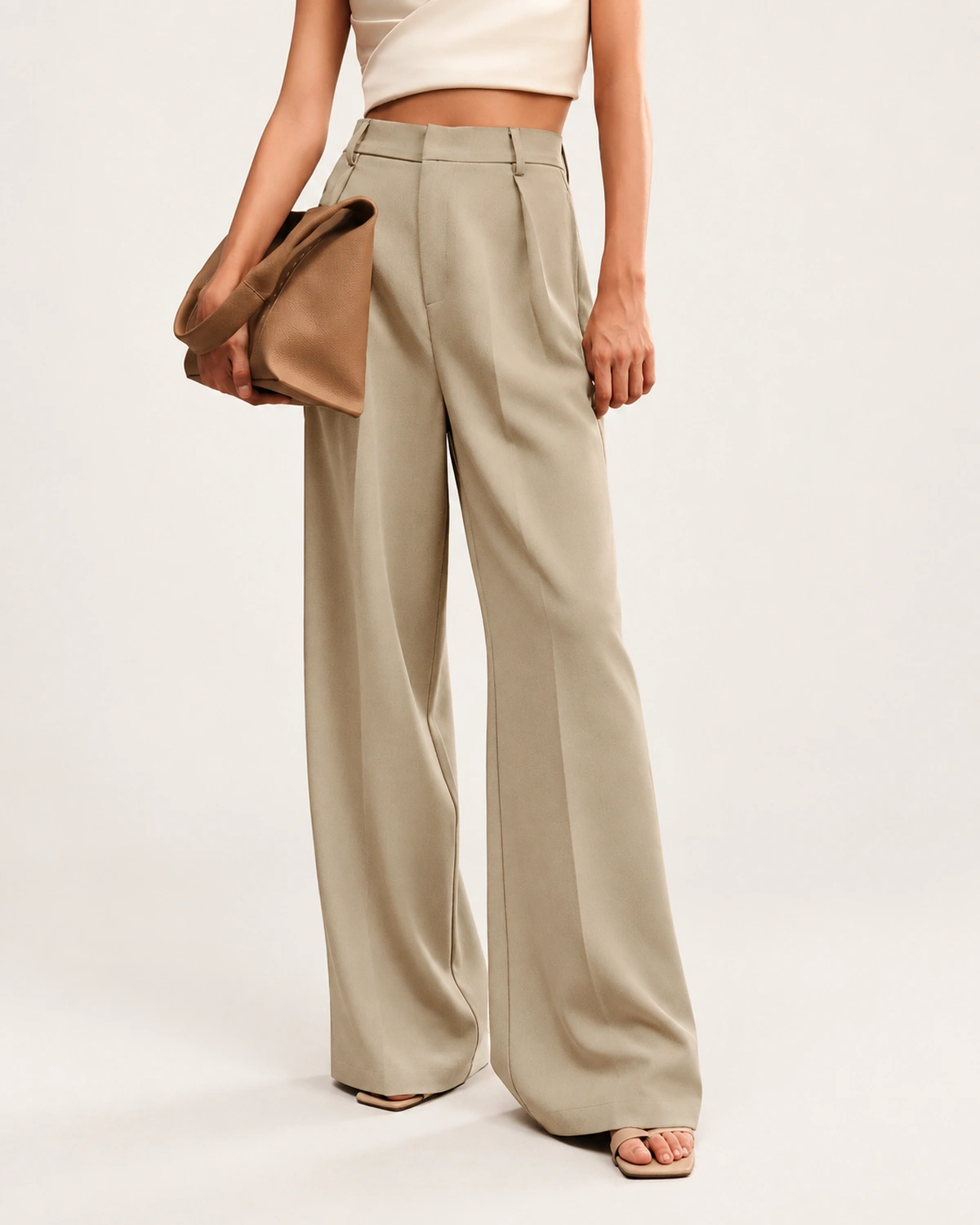 Modelo vestindo calça alfaiataria na cor Areia segurando clutch de couro caramelo sob o braço